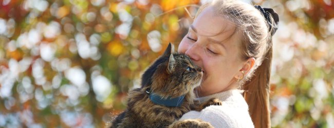 vrouw met bruine kat met GPS-tracker voor katten op halsband buiten en boom op de achtergrond